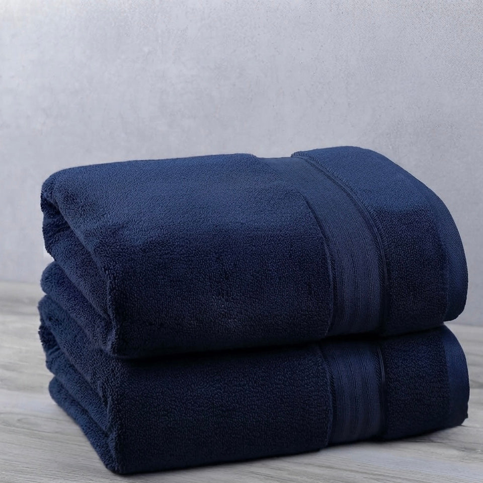 Two folded dark navy blue towels stacked on a light gray wood-textured surface against a textured light gray wall.