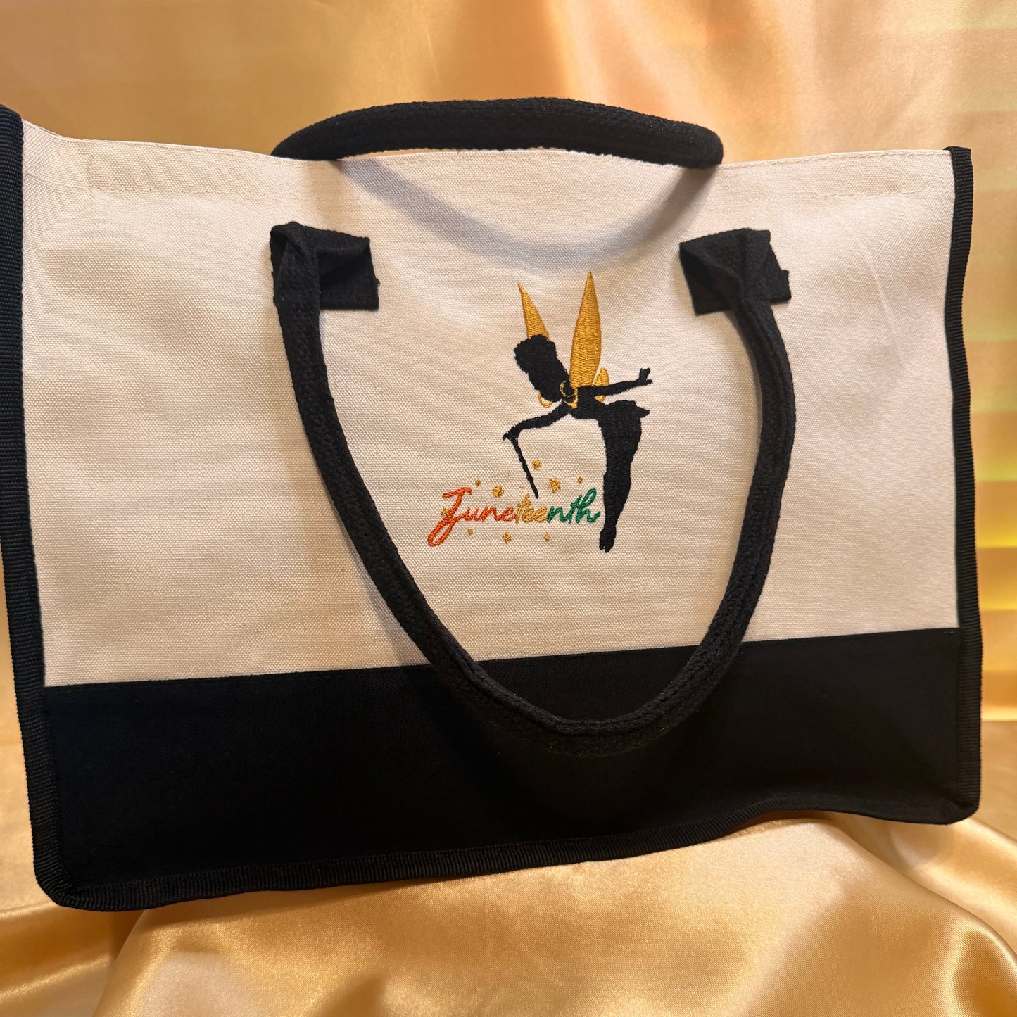 A black and white canvas tote bag with a black handle, featuring a graphic of a martial artist in a black belt stance with a gold sword and the text 'Jiu Jitsu' in orange and green, displayed on a gold satin fabric background.