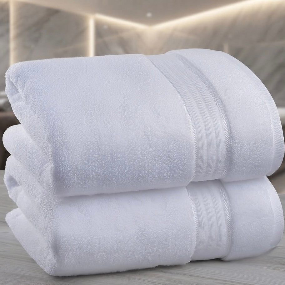 Two folded white bath towels stacked on a light gray marble surface, with a softly blurred modern bathroom background.