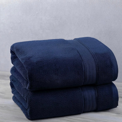 Two folded dark navy blue towels stacked on a light gray wood-textured surface against a textured light gray wall.