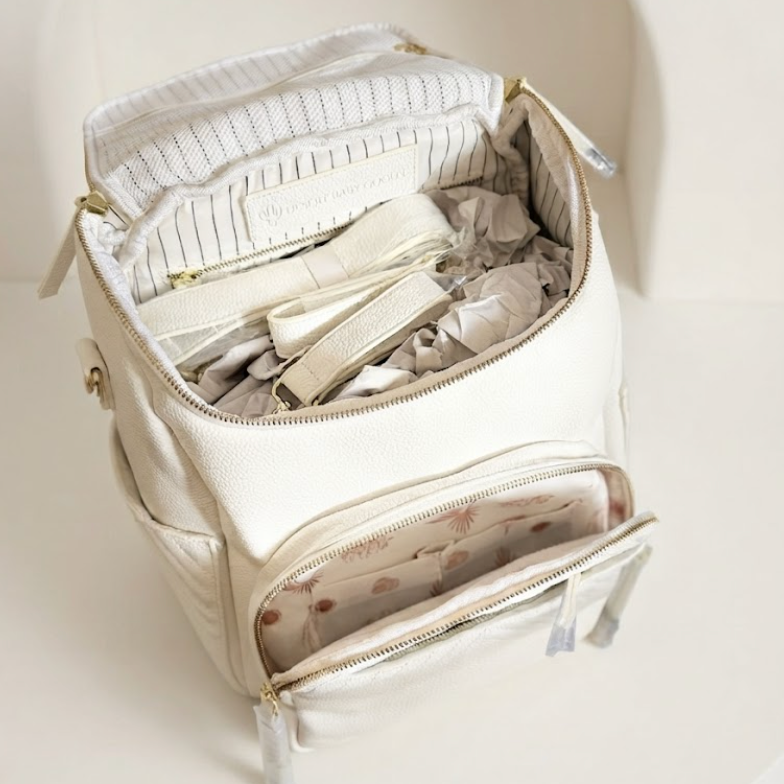 An off-white canvas organizer bag shown open, revealing its interior compartments filled with folded items. The bag features a zippered front pocket and a striped interior lining, photographed against a clean, minimalist cream-colored background.